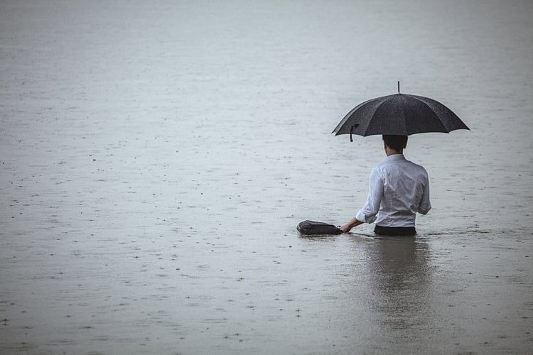 man standing in water and holding umbrella during rain