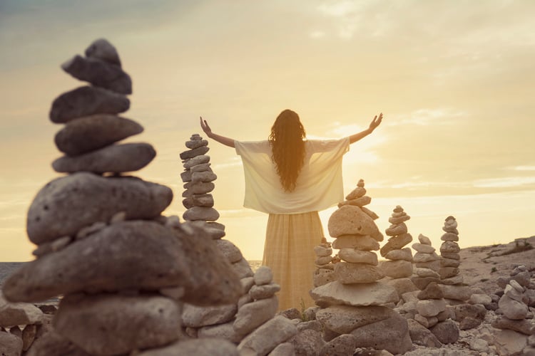 Woman with arms outstretched at sea in the middle of stacked rocks.