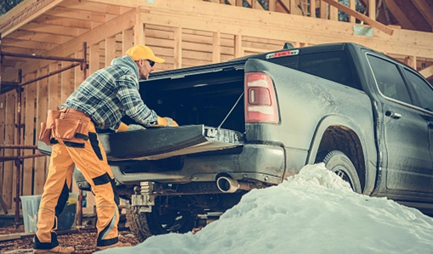 Man looking in the back of his truck with the tailgate down in front of a semi-built house