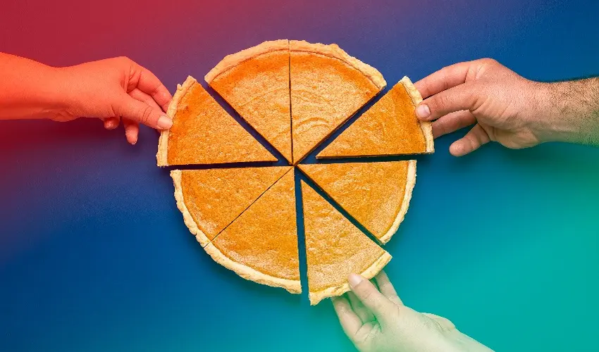 Pumpkin pie cut into eight equal pieces. Three different hands are grabbing slices.